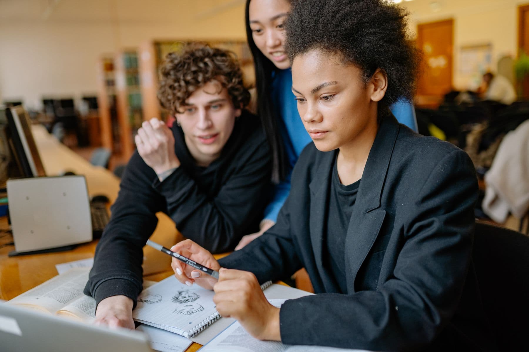 Three students huddled over a laptop in a university library, working something out together