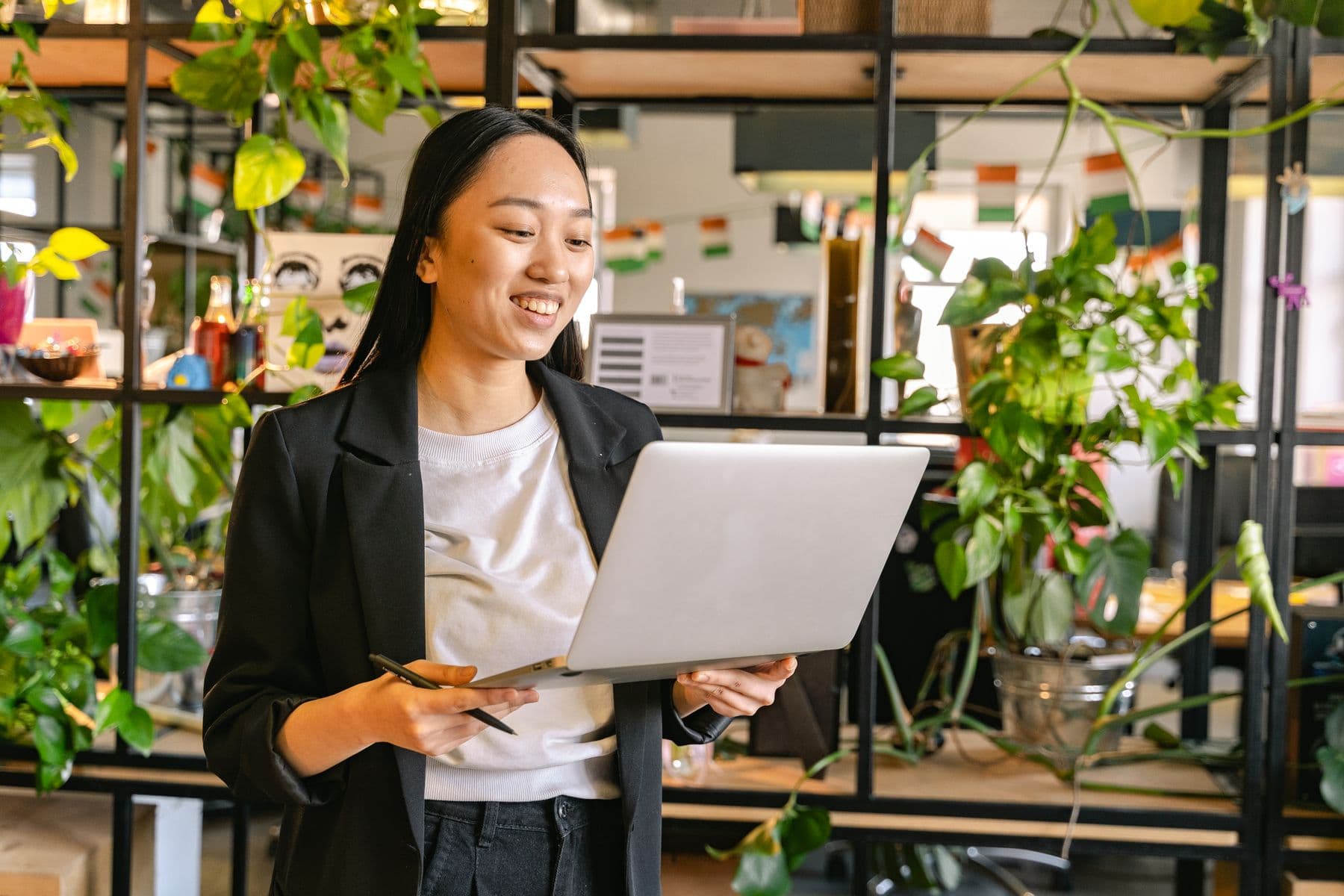 A young professional smiling at her laptop in a plant-filled studio